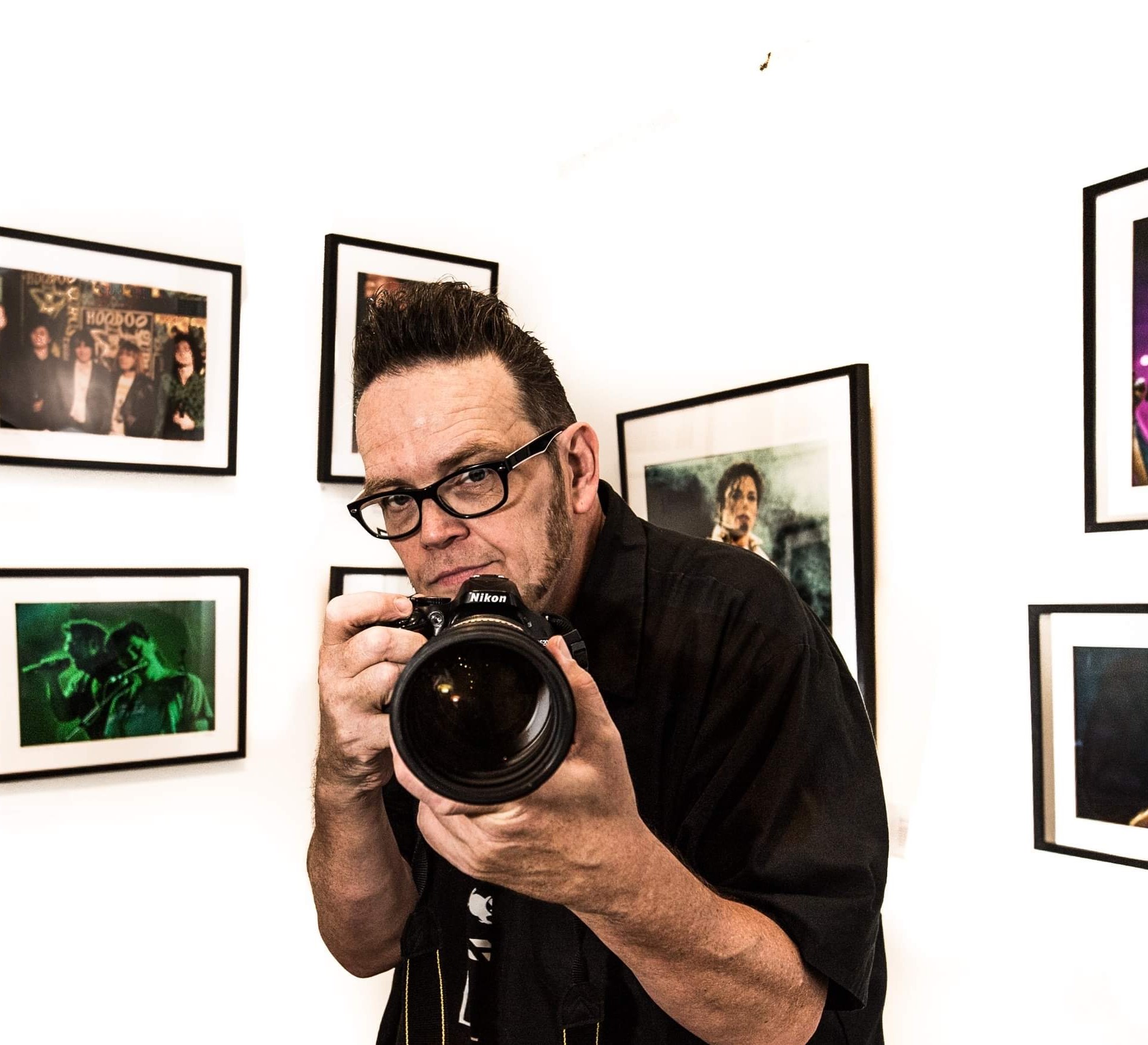 Ian Bell with camera in front of framed photos